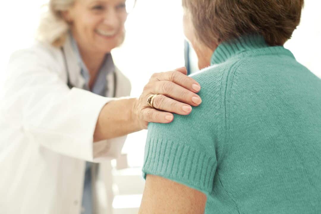 A healthcare provider places her hand on a woman's shoulder.